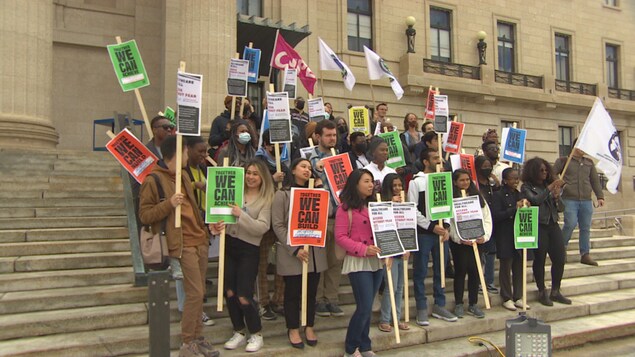Un groupe d'étudiants avec des pancartes devant le Palais législatif du Manitoba.