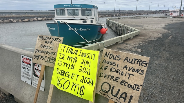 Des affiches devant un bateau de pêche.