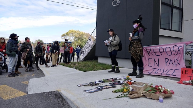 Des personnes prennent la parole devant des photos de femmes disparues ou assassinées et des bouquets de fleurs.