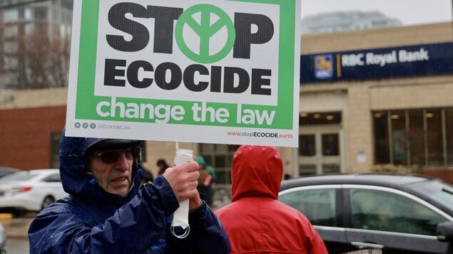 Un homme brandit une pancarte sur laquelle sont écrits les mots « Stop ecocice change the law ».
