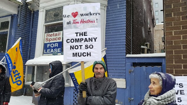 Un manifestant brandit une affiche sur laquelle est écrit en anglais: « Nous aimons les travailleurs de Tim Hortons. La compagnie, pas tant que ça ». Un manifestant brandit une affiche sur laquelle est écrit en anglais: « Nous aimons les travailleurs de Tim Hortons. La compagnie, pas tant que ça ».