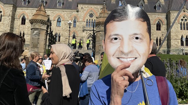 Une personne avec un masque de Volodymyr Zelensky devant le parlement à Ottawa.
