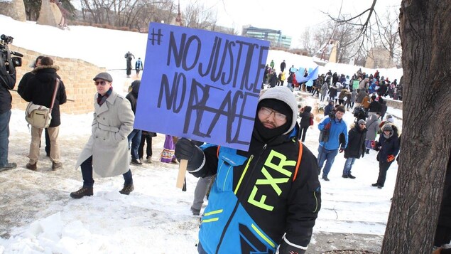 Un manifestant brandit une pancarte réclamant justice et paix lors d'une manifestation dans un parc enneigé à Winnipeg. Un manifestant brandit une pancarte réclamant justice et paix lors d'une manifestation dans un parc enneigé à Winnipeg.