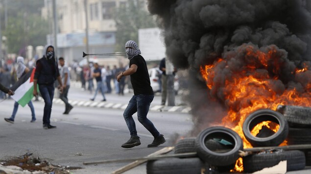 Un Palestinien masqué manie une fronde derrièere un barrage de pneus en feu. Un Palestinien masqué manie une fronde derrièere un barrage de pneus en feu.