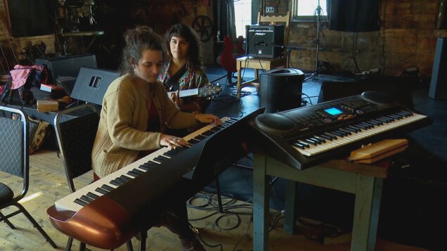 Une musicienne joue au piano, alors qu'une deuxième l'accompagne à la guitare.