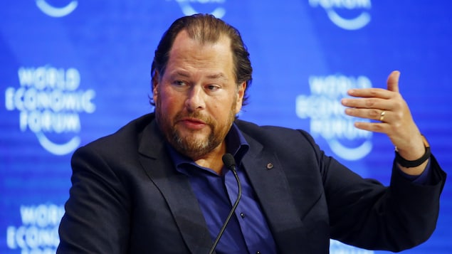 Une photo de Marc Benioff en train de s'exprimer devant un micro. Il porte un veston bleu foncé et une chemise d'un bleu un peu plus pâle.