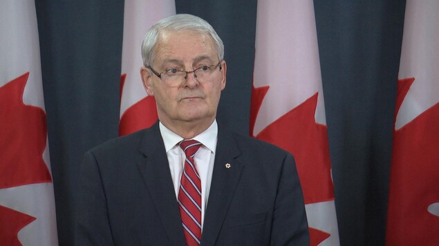 Marc Garneau lors d'une conférence de presse devant des drapeaux canadiens.