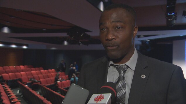Un homme en entrevue avec Radio-Canada avec en arrière plan un auditorium. Un homme en entrevue avec Radio-Canada avec en arrière plan un auditorium.