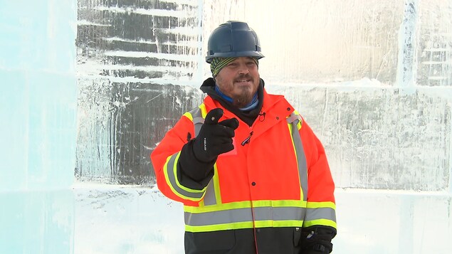Marc Lepire, l'artisan derrière le palais de glace de Bonhomme Carnaval en tenu de construction, devant un mur de glace. 