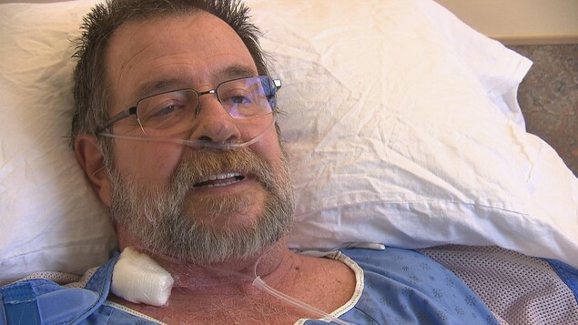 Une homme portant des lunettes en entrevue dans sa chambre d'hôpital.