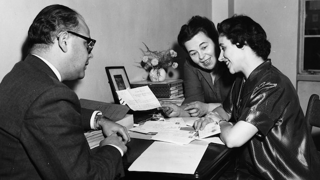 Dans un bureau, Claude Mailhiot, Marcelle Barthe et Magdeleine Mailhiot, sont assis à une table et dépouillent le courrier, en discutant. Dans un bureau, Claude Mailhiot, Marcelle Barthe et Magdeleine Mailhiot, sont assis à une table et dépouillent le courrier, en discutant.