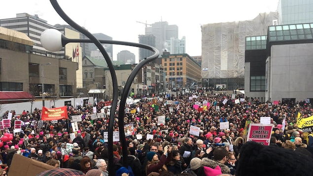 Une foule, dans laquelle on distingue plusieurs pancartes et chapeaux roses, est rassemblée à la Place des Arts, à Montréal.