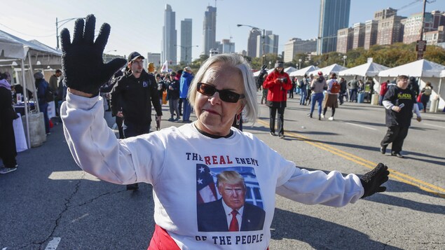 Une femme montre son opposition à Donald Trump en portant un chandail sur lequel est inscrit « Le vrai ennemi du peuple ». En arrière d'elle, d'autres marcheurs commencent à se rassemble. En arrière-plan, des bâtiments du centre-ville de Chicago. Une femme montre son opposition à Donald Trump en portant un chandail sur lequel est inscrit « Le vrai ennemi du peuple ». En arrière d'elle, d'autres marcheurs commencent à se rassemble. En arrière-plan, des bâtiments du centre-ville de Chicago.