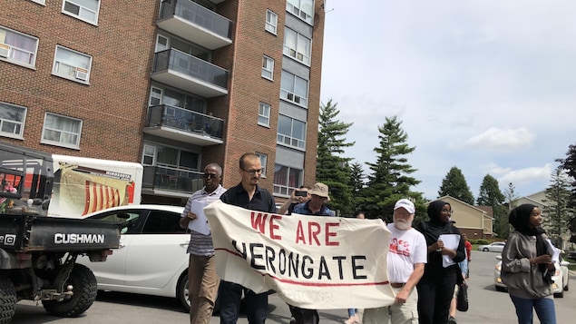 Des manifestants tiennent une affiche où le slogan «We are Heron Gate» («Nous sommes Heron Gate») est inscrit.