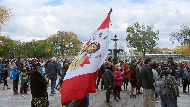 Gros plan sur un drapeau autochtone dans une manifestation. On voit plusieurs personnes derrière.