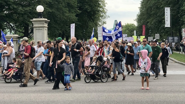 Plusieurs personnes marchent dans les rues de Québec et quelques drapeaux flottent dans les airs.