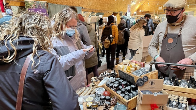 Des gens regardent des produits de soin des cheveux sur une table d'un marchand dans un marché de Noël.