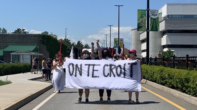 Des manifestantes masquées, poing levé, qui tiennent une banderole sur laquelle est écrit : "On te croit". Elles marchent tout près du lieu de départ, sur le campus de l'UQTR.