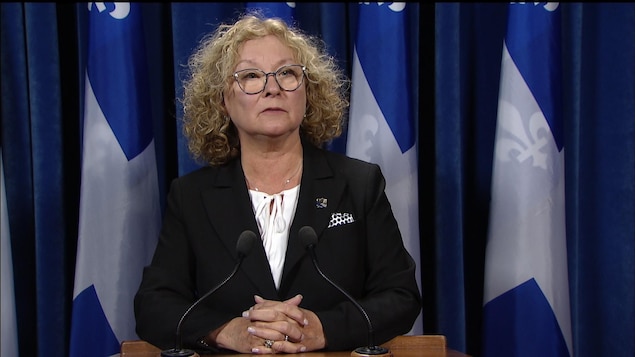 Marguerite Blais en point de presse, devant des drapeaux du Québec