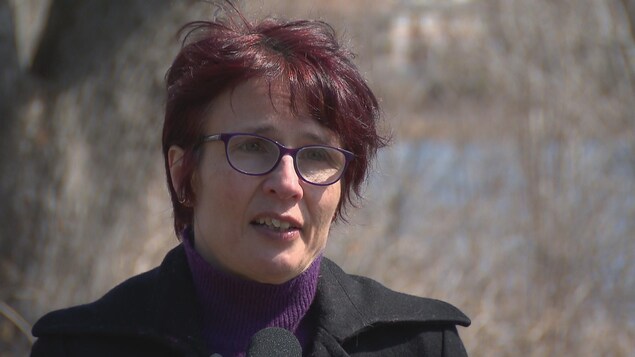 Marie Blouin en entrevue devant une rivière bordée d'arbres.