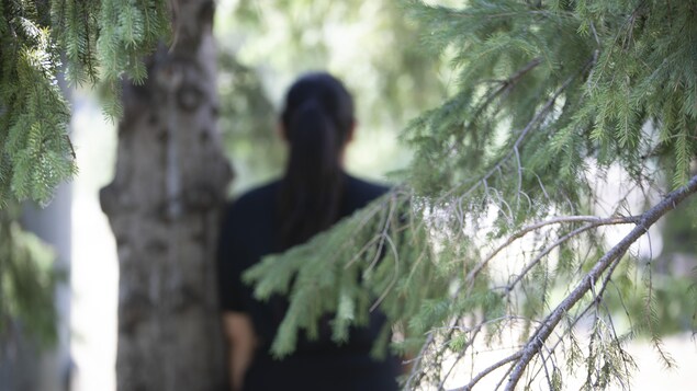Une fille de dos prend appui sur un arbre dans un parc.