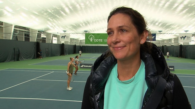 Marie-Ève Pelletier sourit devant la caméra avec des terrains de tennis et des joueurs en arrière-plan.