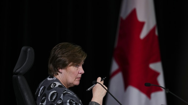 Marie-Josée Hogue, assise devant un drapeau du Canada, jette un coup d'œil de côté vers la salle.