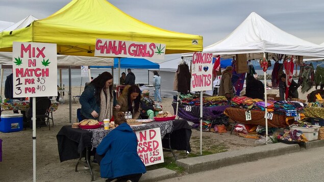 Trois femmes autour d'une table ont des biscuits à la marijuana à vendre sur la plage Sunset lors du 4/20 organisé à Vancouver en avril 2018.