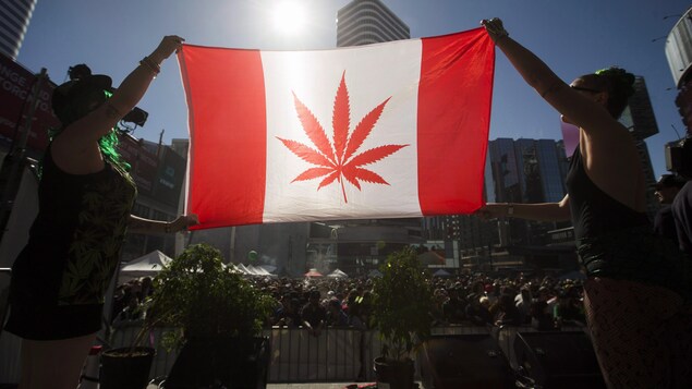 Deux femmes tiennent un drapeau du Canada où la feuille d'érable a été remplacée par celle de la marijuana