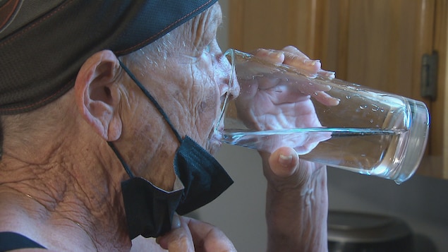 Une femme aînée boit un verre d’eau. 