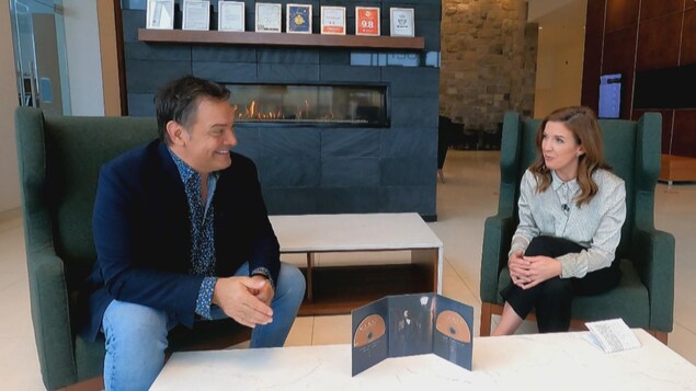 Mario Pelchat en entrevue avec Mélanie Patry dans le hall d'un hôtel.