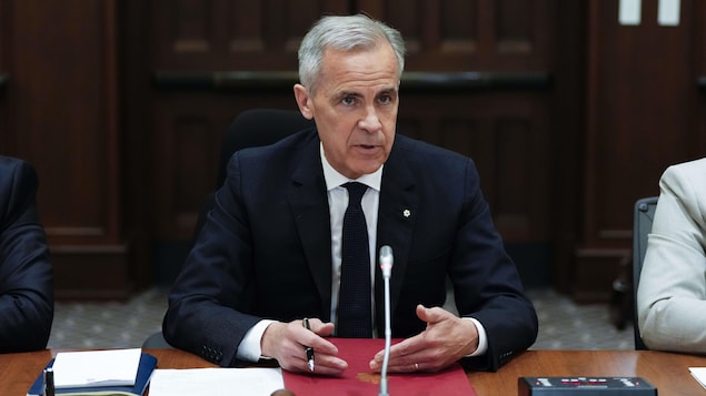 Mark Carney signe un document devant la presse.