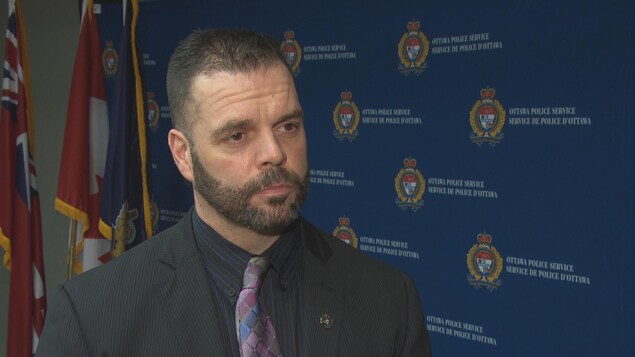 Mark Patterson donne une entrevue à Radio-Canada dans les locaux du Service de police d'Ottawa, alors qu'en arrière-plan se trouvent plusieurs logos du SPO. Mark Patterson donne une entrevue à Radio-Canada dans les locaux du Service de police d'Ottawa, alors qu'en arrière-plan se trouvent plusieurs logos du SPO.