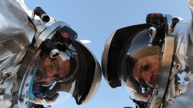 Vue rapprochée et en contre-plongée des visages des deux scientifiques, portant des combinaisons spatiales, regardant vers le sol. Vue rapprochée et en contre-plongée des visages des deux scientifiques, portant des combinaisons spatiales, regardant vers le sol.