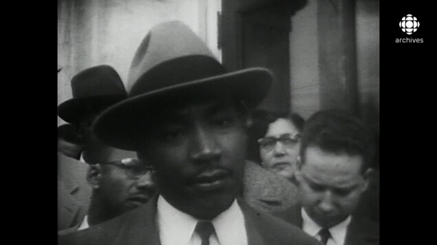Martin Luther King, portant chapeau et habit, entouré de partisans. Martin Luther King, portant chapeau et habit, entouré de partisans.