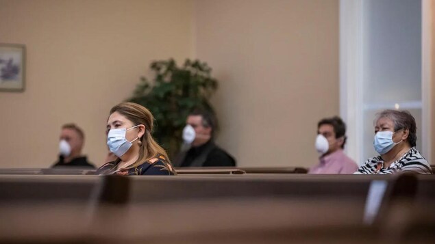 Un groupe de personnes portant un masque assistent à une célébration religieuse.
