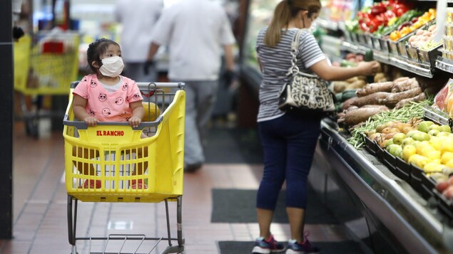 Une petite fille et sa mère portent des masques en faisant l'épicerie.