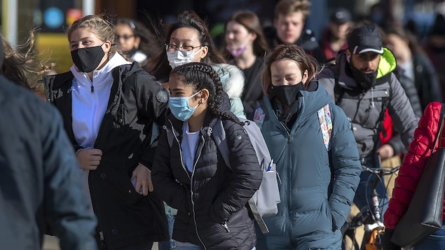 Un groupe de gens marchent sur un trottoir. Une personne est à vélo.