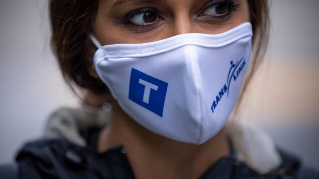 Une femme porte un masque à l'effigie de la Société des transports de Vancouver, TransLink.