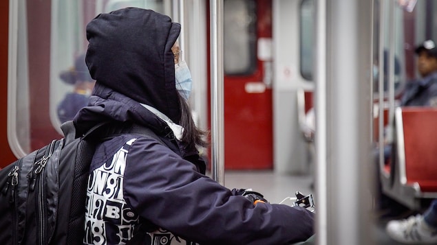Une femme portant un masque est assise dans le métro de Toronto.