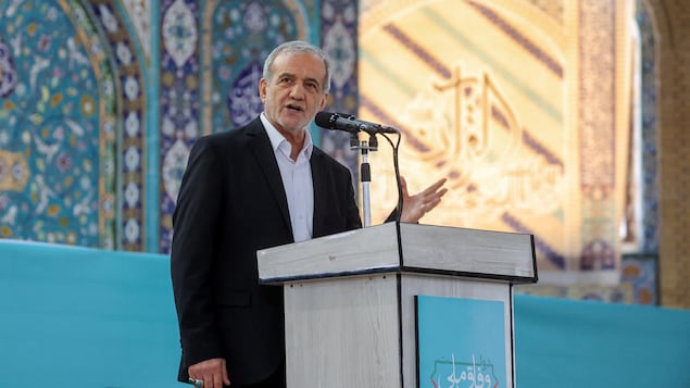 Massoud Pezeshkian speaks on stage in front of a microphone.