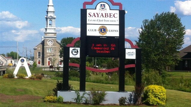 L'église de Sayabec avec une affiche aux couleurs de la municipalité en avant-plan.
