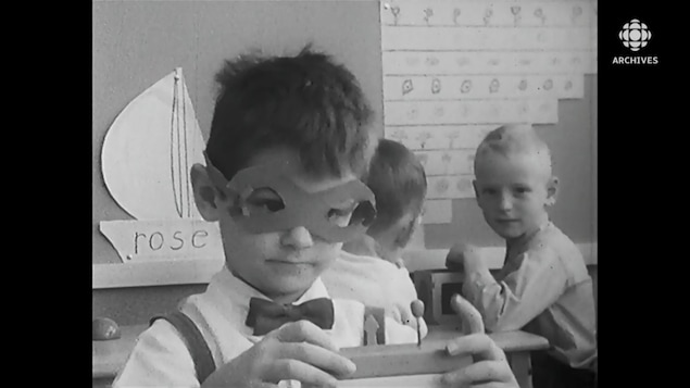 Un garçon, masque de papier sur les yeux, s'amuse avec des blocs dans une classe de maternelle.