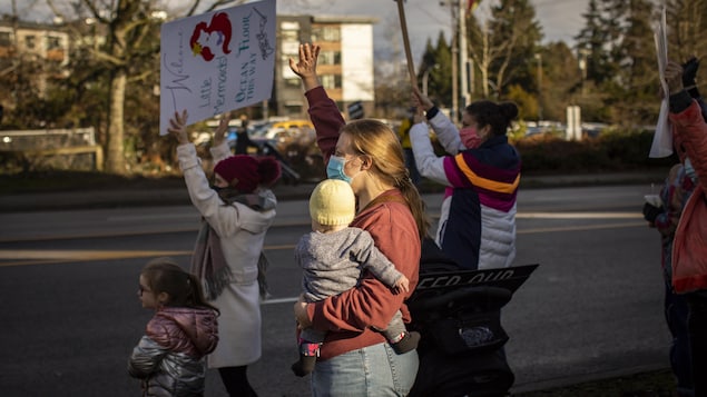 Une maman entourée de manifestantes tient son bébé dans un bras et lève l'autre main en l'air. 