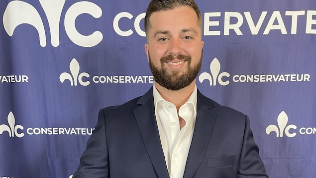 Matthieu Kadri pose devant une bannière du Parti conservateur du Québec.