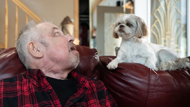 On voit M. Desjardins, assis, de profil, qui regarde son chien couché sur le divan.