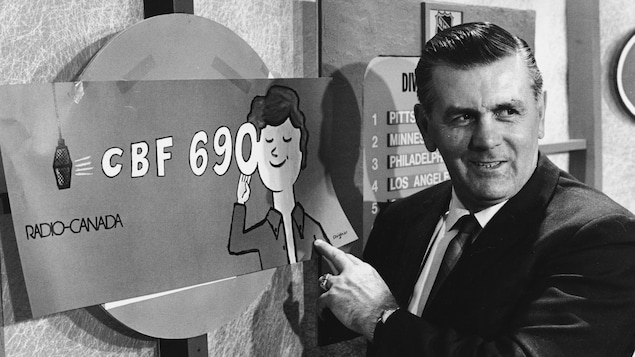 Dans un studio de radio, l'ancien joueur de hockey Maurice Richard pointe une affiche publicitaire de la station CBF 690.