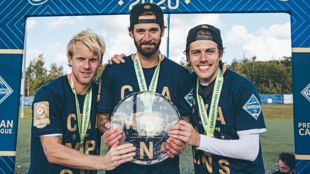 Trois joueurs de soccer tiennent le trophée de la Première ligue candienne de soccer