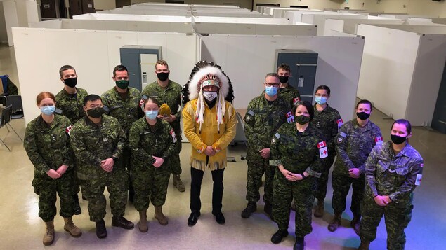 Le chef, en habits traditionnels, se tient au milieu du groupe de soldats. Tous portent un masque.