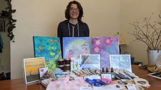 Jordynn Friesen se tient derrière une table sur laquelle sont posés les objets recueillis, notamment des tableaux de peinture, des bracelets, des pots de confiture et des produits de soins corporels.